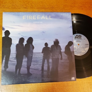 May include: A vinyl record and album cover for the band Firefall's album "Undertow." The album cover features a group of silhouetted figures standing on a beach with a blue and purple sky. The record is black.