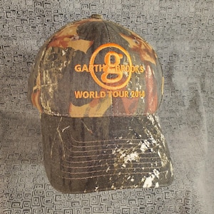 Peut inclure: Une casquette de baseball camouflage avec un logo brod&eacute; orange qui dit "Garth Brooks World Tour 2014".