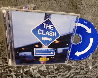 May include: A CD case with a blue and white design featuring a road sign that says "The Clash" and "From Here To Eternity". The CD case is open and the CD is visible. The CD is blue with a white arrow.