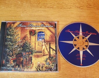 May include: A Trans-Siberian Orchestra The Christmas Attic CD in a plastic case with cover art depicting a child in an attic with a Christmas tree and toys, alongside the blue disc featuring a white star design and the album title text.