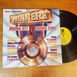 May include: A vinyl record album titled Winners, featuring a gold record graphic and a list of artists including Barry Manilow, Boston, and Meatloaf. The cover displays the text Ronco presents, Original Hits, Original Stars, and As Seen On TV.
