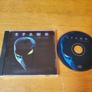 May include: A CD case and disc for the album "Spawn: The Album." The case and disc feature a blue and black graphic of the Spawn character. The CD case is black and the disc is dark blue.