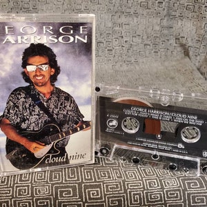 May include: A cassette tape of George Harrison's album "Cloud Nine". The album cover features a photo of George Harrison playing a guitar. The cassette tape is in a clear plastic case.