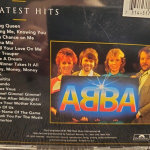 May include: ABBA's Greatest Hits CD. The album cover features the band members and the ABBA logo in blue and yellow. The tracklist includes popular songs like "Dancing Queen" and "Mamma Mia".
