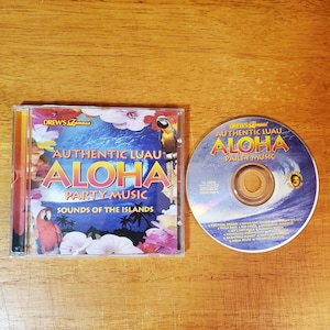 May include: A CD case and disc featuring the album "Authentic Luau Aloha Party Music: Sounds of the Islands." The case has a colorful design with flowers, parrots, and the album title. The disc has a wave design.
