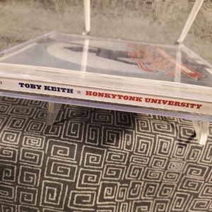 Może przedstawiać: Zbliżenie na pudełko CD z białym tłem i czerwonym tekstem. Tekst brzmi "Toby Keith Honkytonk University" i "Dreamworks".