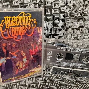 May include: A cassette tape with a black and white image of a band called Electric Boys. The tape is labeled "Funk-O-Metal Carpet Ride" and features the song titles "Psychedelic Eyes", "All Lips & Hips Change", "I Had A Car", and "Captain Of My Soul".