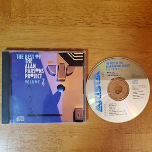 May include: A CD case and disc for "The Best of The Alan Parsons Project Volume 2." The case is blue with abstract art and text. The disc is silver with the album title and track listing.