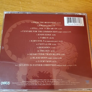 May include: A compact disc case with a maroon-colored insert featuring a tracklist and a stylized illustration. The disc's barcode is visible. The text includes song titles and the word "Chronicles".