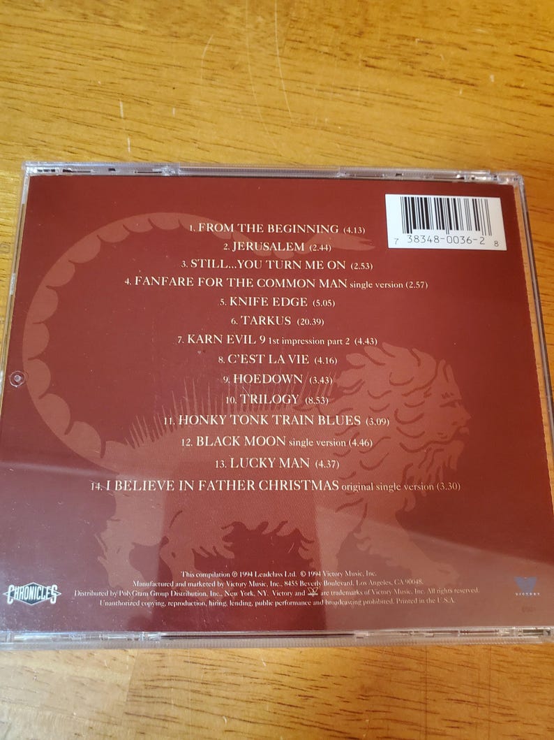 May include: A compact disc case with a maroon-colored insert featuring a tracklist and a stylized illustration. The disc's barcode is visible. The text includes song titles and the word "Chronicles".