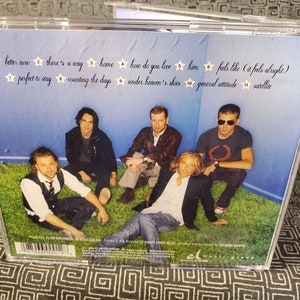 May include: A CD case with a blue background and a group of five men posing on a green lawn. The back of the case lists the track titles and song names: "better now", "there's a way", "home", "how do you love", "him", "feels like (it feels alright)", "perfect to stay", "counting the days", "under heaven's skies", "general attitude", "satellite".