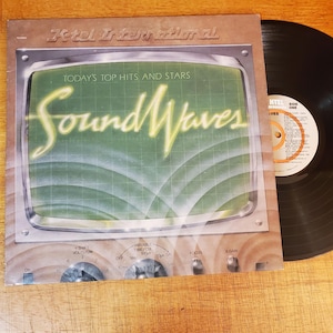 May include: A K-tel International vinyl record album titled Sound Waves, featuring a graphic of an oscilloscope screen with green grid lines and yellow text. The cover includes control knobs labeled Y Shift, Volts/CM, and Variable Time/CM.