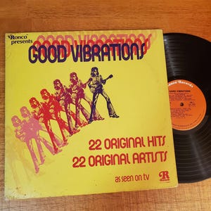 May include: A yellow vinyl record sleeve titled Good Vibrations by Ronco, featuring a graphic of musicians in red and blue. The text reads 22 Original Hits, 22 Original Artists, and as seen on tv. A black vinyl record with an orange label is visible.