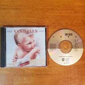 May include: A CD case and disc featuring the band Van Halen. The CD case displays a cherubic figure with wings. The disc has the band's name and track listing. The album was produced by Ted Templeman.