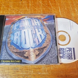 May include: A CD case with a blue and gold design featuring the text "Petra Means Rock" and "17 Thundering Rock Classics".