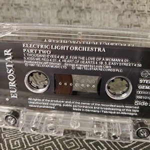 May include: A black cassette tape with a clear plastic case. The tape is labeled "Electric Light Orchestra Part Two" and features the song titles "Thousand Eyes", "For the Love of a Woman", "Kiss Me Red", "Heart of Hearts", and "Easy Street". The tape is labeled "Side 2" and has a "Stereo" and "GEMA" logo.