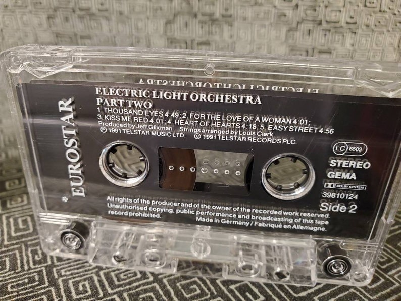 May include: A black cassette tape with a clear plastic case. The tape is labeled "Electric Light Orchestra Part Two" and features the song titles "Thousand Eyes", "For the Love of a Woman", "Kiss Me Red", "Heart of Hearts", and "Easy Street". The tape is labeled "Side 2" and has a "Stereo" and "GEMA" logo.