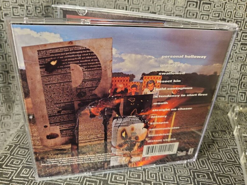 以下が含まれることがあります： 画像とテキストのコラージュが施された音楽CDの背面。テキストには、「personal holloway」、「greedy ay」、「swallowed」、「insect kin」、「cold contagious」、「tendency to start fires」、「mouth」、「straight no chaser」、「history」、「synapse」、「communicator」、「home driver」、「distant voices」などの言葉が含まれています。