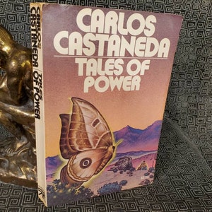 May include: A vintage paperback book titled "Carlos Castaneda Tales of Power" with a brown and white butterfly on the cover. The background is a desert landscape with a sunset.