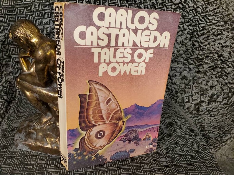 May include: A vintage paperback book titled "Carlos Castaneda Tales of Power" with a brown and white butterfly on the cover. The background is a desert landscape with a sunset.