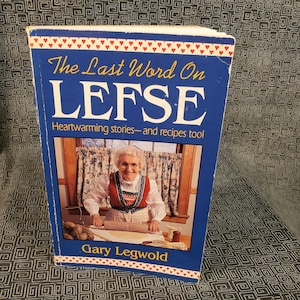 May include: A blue book with the title "The Last Word On Lefse" and a subtitle "Heartwarming stories - and recipes too!"  The book features a photo of a woman in a red and white apron making lefse.