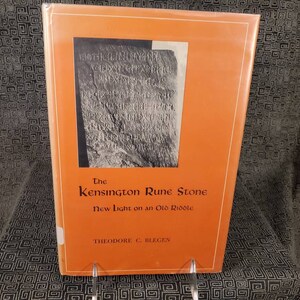 May include: An orange book cover with a black and white photo of a stone with runic inscriptions. The title of the book is "The Kensington Rune Stone: New Light on an Old Riddle" by Theodore C. Blegen.