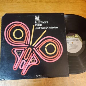 May include: A vintage vinyl record album by the Five Man Electrical Band, titled "good-byes & butterflies." The album cover is black with a neon-style butterfly design in pink, orange, and yellow. A black vinyl record is visible next to the album.