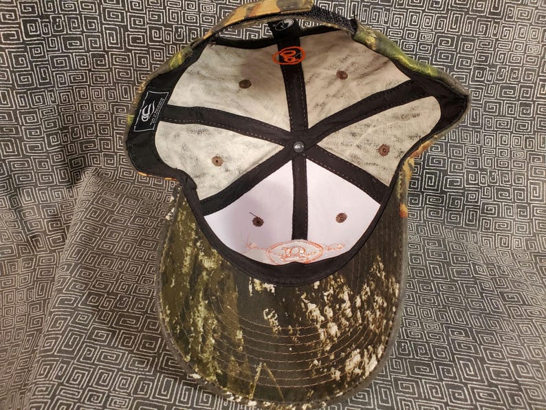 Peut inclure: Une casquette de baseball camouflage avec une visi&egrave;re noire et un dos en maille blanche. L'int&eacute;rieur de la casquette est blanc avec des coutures noires et un petit logo orange. La casquette a une fermeture velcro.