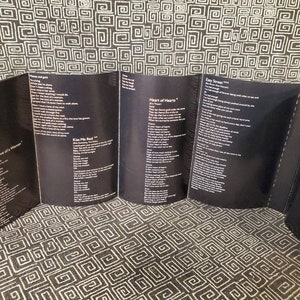 May include: A black and white cassette tape case with lyrics printed on the inside. The lyrics include the song titles "For the Love of a Woman", "Kiss Me Real", "Heart of Hearts", and "Easy Street".