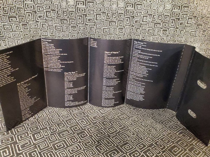 May include: A black and white cassette tape case with lyrics printed on the inside. The lyrics include the song titles "For the Love of a Woman", "Kiss Me Real", "Heart of Hearts", and "Easy Street".
