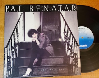 May include: Album cover for Pat Benatar's "Precious Time" LP. The cover features a black and white photo of a woman sitting on stairs. The album title and artist's name are printed in white. A black vinyl record is visible.