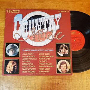 May include: A red vinyl record album cover titled The 15th Annual Academy of Country Music Awards, featuring portraits of four artists and a list of 16 performers including Charlie Rich and Linda Ronstadt. A black vinyl record is partially visible.