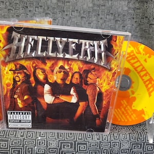 May include: CD of the band Hellyeah, featuring a group of men in front of a fiery background. The CD case is clear, and the disc is yellow and orange. The album cover has the Parental Advisory Explicit Content warning.