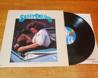 May include: The album cover for "Sweet Dreams" shows a couple in a car, with the title in turquoise script. A black vinyl record is next to the cover, with a rainbow label. The album is "The Life and Times of Buddy Holly."
