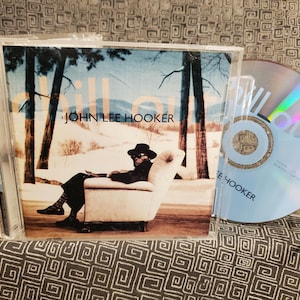 May include: A CD case with a photo of a man sitting in a chair. The CD case is titled "Chill Out" and features the artist John Lee Hooker.