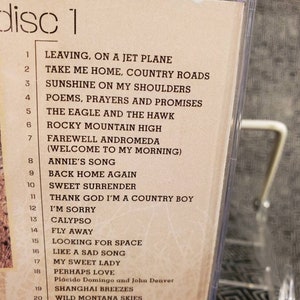 May include: A beige CD insert labelled disc 1, listing 20 tracks including Leaving, On A Jet Plane, Take Me Home, Country Roads, Sunshine On My Shoulders, Poems, Prayers And Promises, The Eagle And The Hawk, Rocky Mountain High, and others.