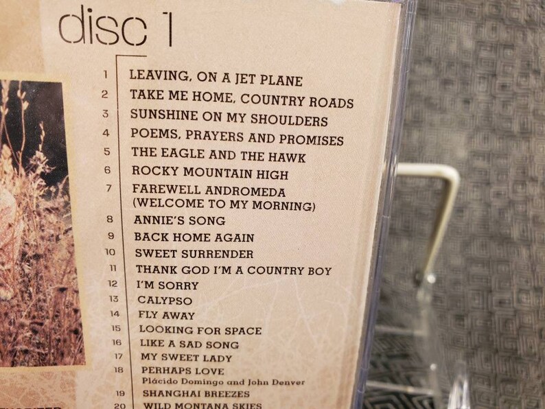 May include: A beige CD insert labelled disc 1, listing 20 tracks including Leaving, On A Jet Plane, Take Me Home, Country Roads, Sunshine On My Shoulders, Poems, Prayers And Promises, The Eagle And The Hawk, Rocky Mountain High, and others.