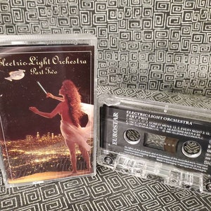 May include: A cassette tape with a black and white label. The label has the text "Electric Light Orchestra Part Two" and a list of song titles. The cassette tape is in a clear plastic case.