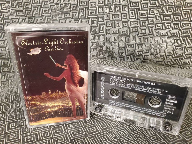 May include: A cassette tape with a black and white label. The label has the text "Electric Light Orchestra Part Two" and a list of song titles. The cassette tape is in a clear plastic case.