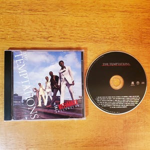May include: A CD case and disc featuring The Temptations. The CD case displays a group of men in suits against a blue sky background. The disc is black with the band's name in white text.