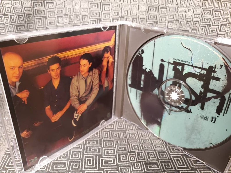 以下が含まれることがあります： 前面に3人の写真、背面に白黒のデザインが施されたCDが入ったCDケース。CDには「INTD-90091」と「BUSH」の文字が書かれている。
