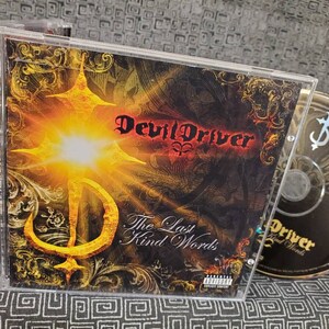 May include: A CD case with a black and gold design. The front cover features the band name "Devil Driver" in red text and the album title "The Last Kind Words" in black text. The background is a dark, textured image with a golden cross and a bright light shining through it.
