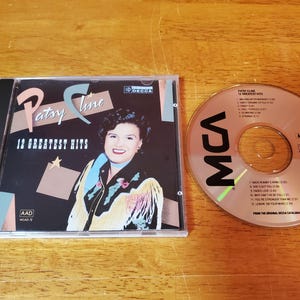 May include: A Patsy Cline "12 Greatest Hits" CD album in a jewel case, next to the CD. The album cover features a portrait of Patsy Cline. The CD has the MCA logo and song titles.