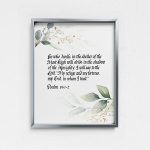 以下が含まれることがあります： 銀色のフレームに入ったプリントで、詩篇91:1-2のエレガントなカリグラフィーが特徴です。テキストは白い背景に配置され、緑と金の水彩画風の植物のアクセントで飾られています。家の装飾用の装飾品です。