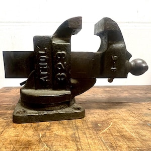May include: A vintage cast iron vise with a black finish. The vise is labeled "S25" and "NORTH" on the side. The vise is mounted on a wooden surface.