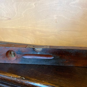 May include: A vintage wooden level with a metal bubble level. The level is dark brown with a reddish brown strip in the center. The level is about 15 inches long.