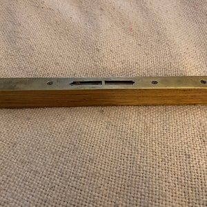 May include: A brass level with a wooden base. The level has two small holes on each side and a rectangular window in the center.