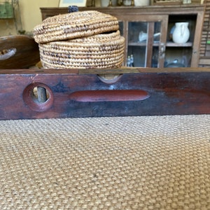 Puede incluir: Un nivel de madera vintage con un nivel de burbuja de latón. El nivel es de color marrón oscuro con una franja roja y un agujero circular en el lateral.