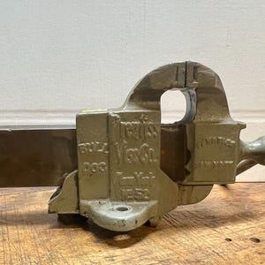 May include: A vintage cast iron vise with a gray finish. The vise has a swivel base and a lever handle. The vise is labeled "Tru-Grip" and "E.Y. Co. 1933".