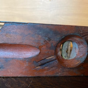 May include: A vintage wooden level with a brass bubble level. The level is dark brown and has a worn finish. The bubble level is circular and has a brass rim.
